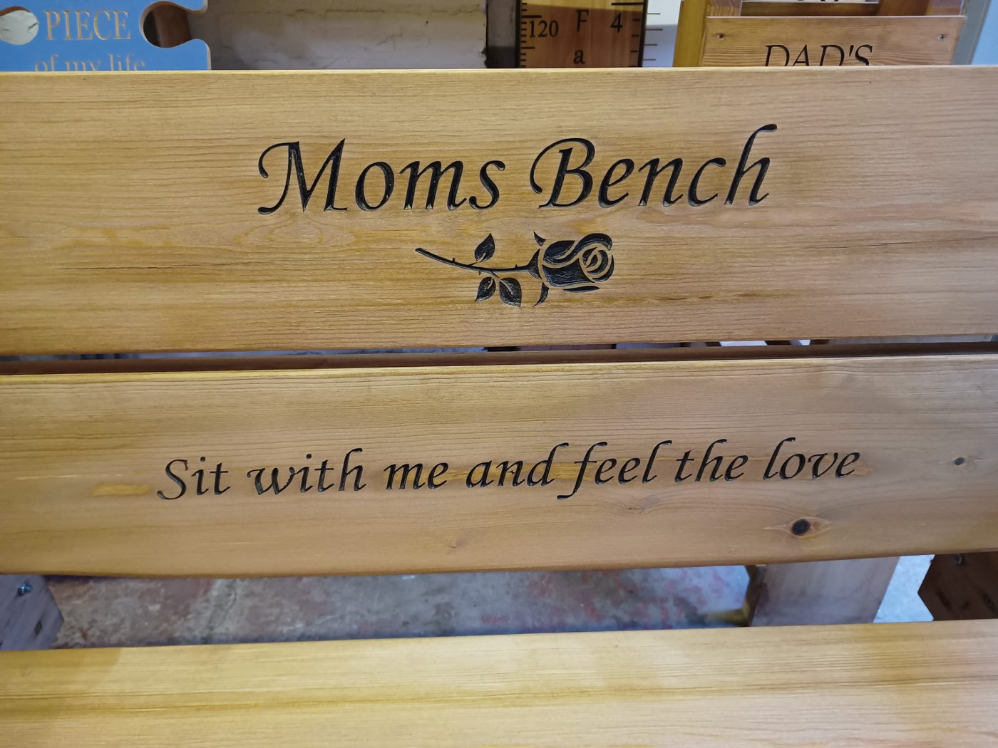 Close-up of carved lettering and a rose on a bench backrest